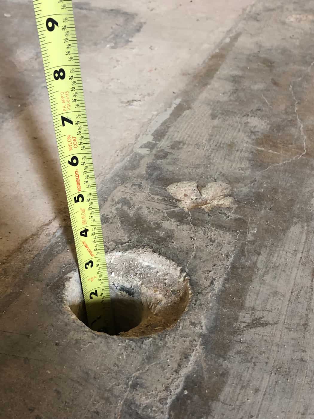 Tape measure in a core hole showing the thickness of a floor slab.
