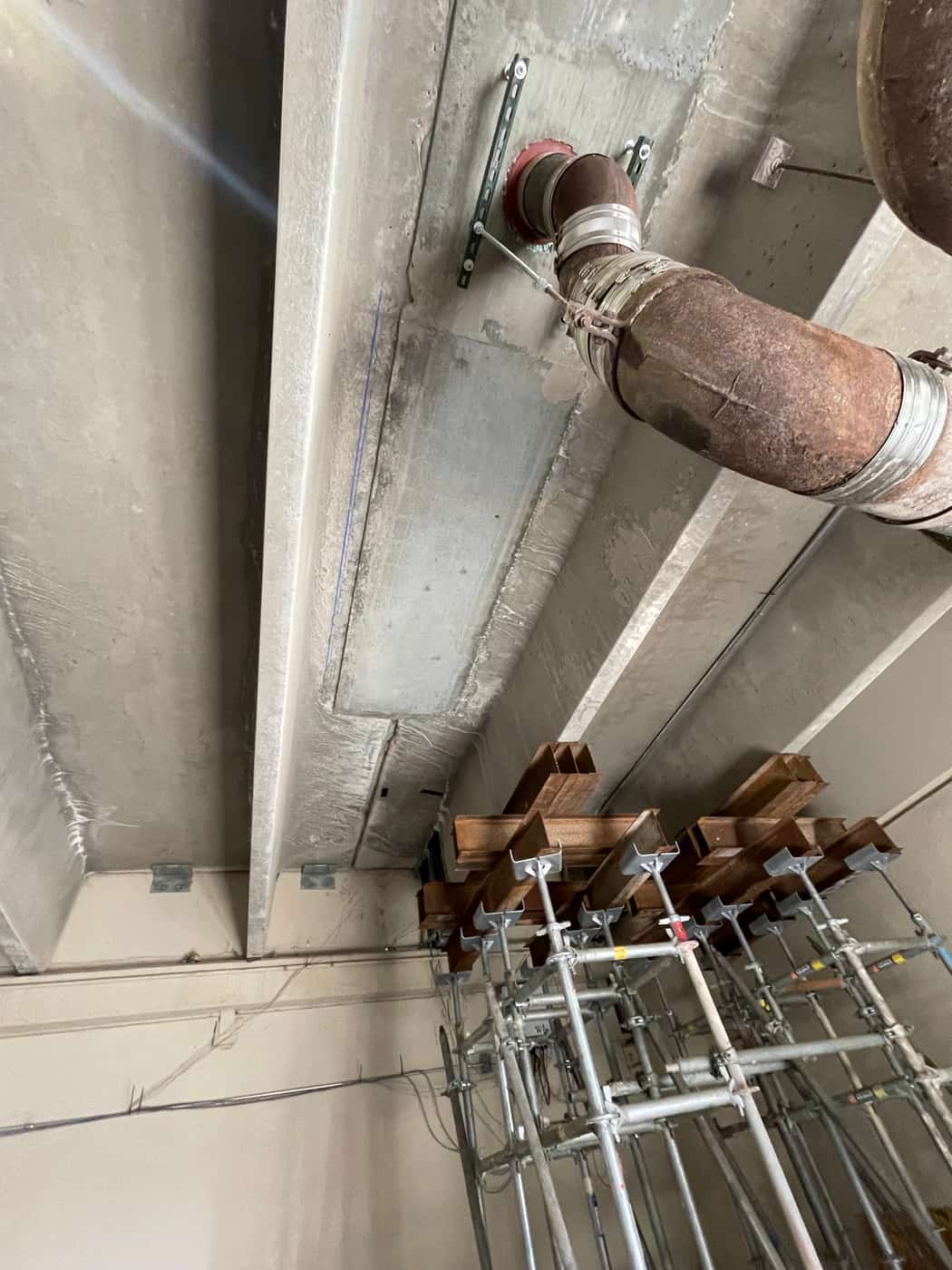 Beam soffit with a steel bracket and pipe beside a shoring tower with cribbing.