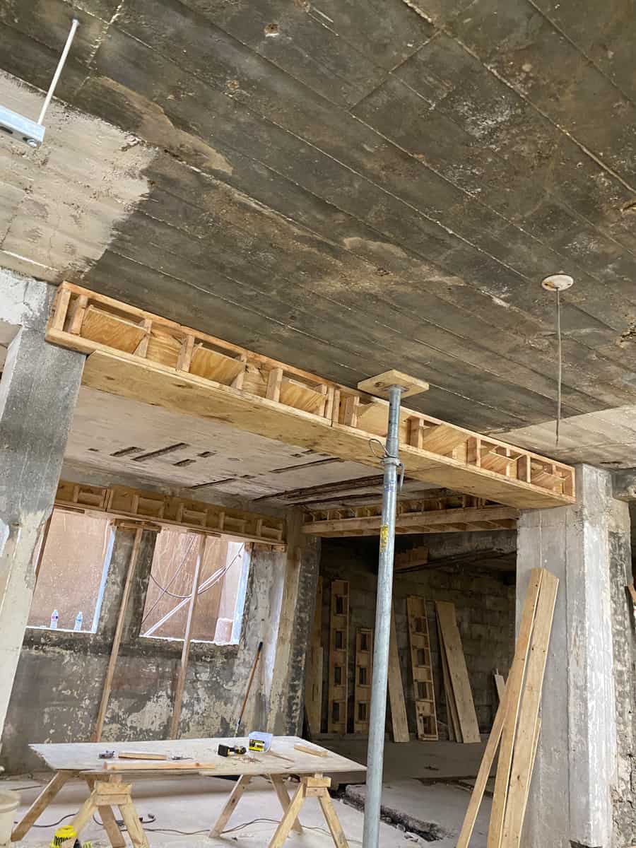 Timber shoring beam on a post under a deteriorated concrete slab in an old basement.