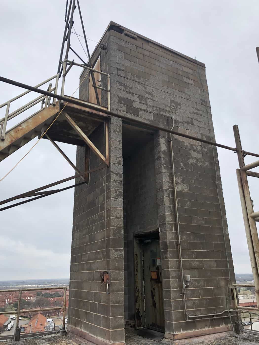 Weathered concrete masonry stair tower on a plant rooftop with a steel access stair.