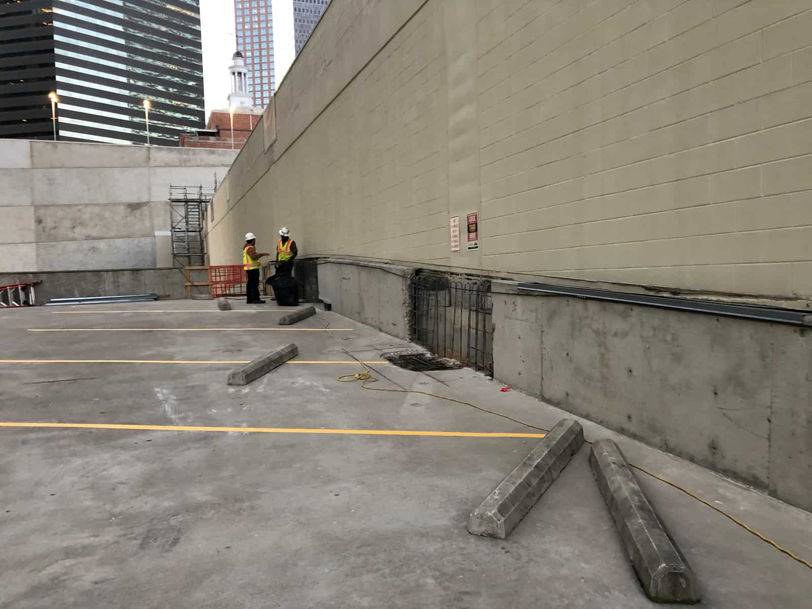 Rooftop parking deck wall line with workers and concrete debris.