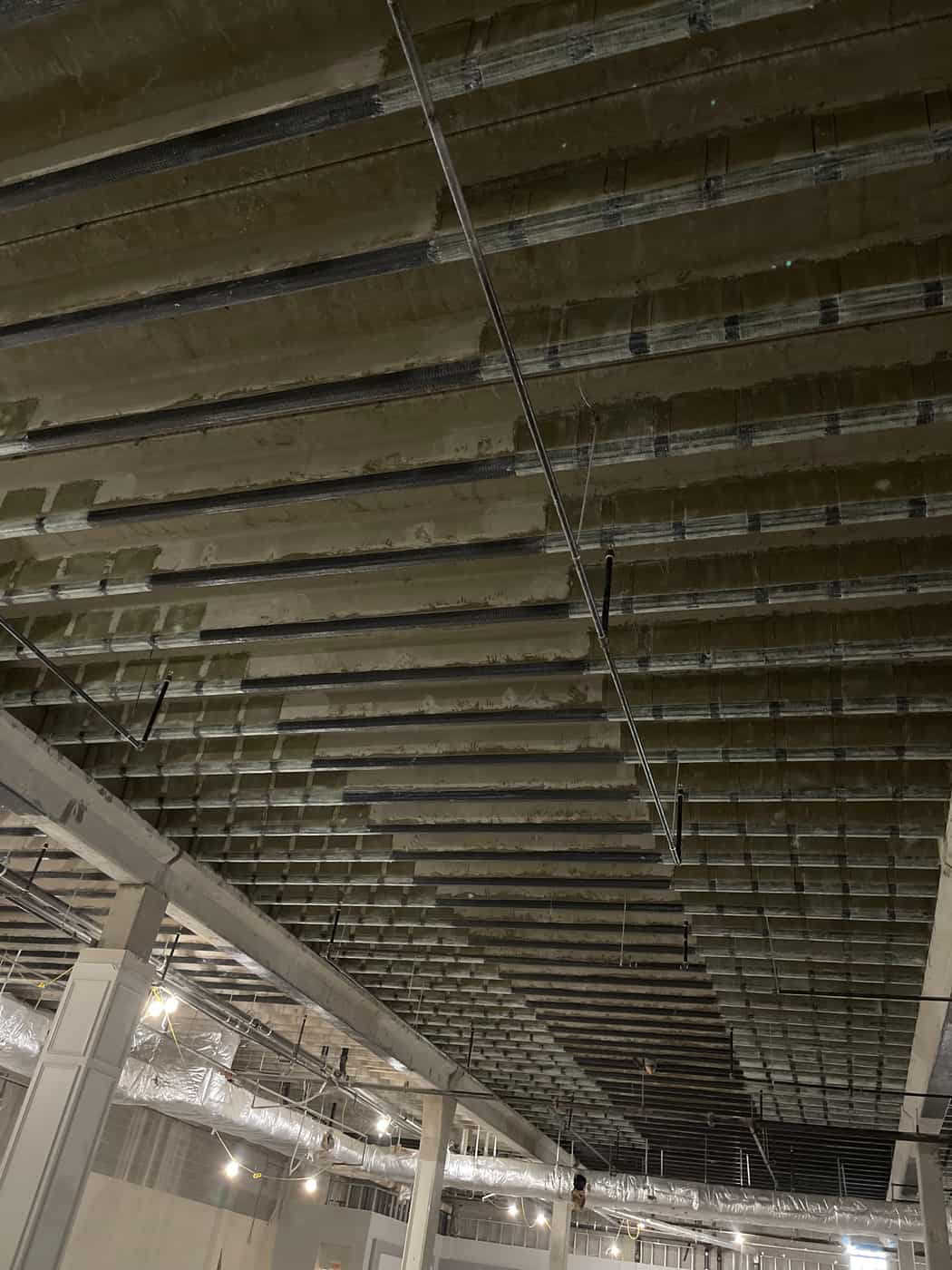 Pan-joist ceiling with carbon fiber bands above a large renovation space.