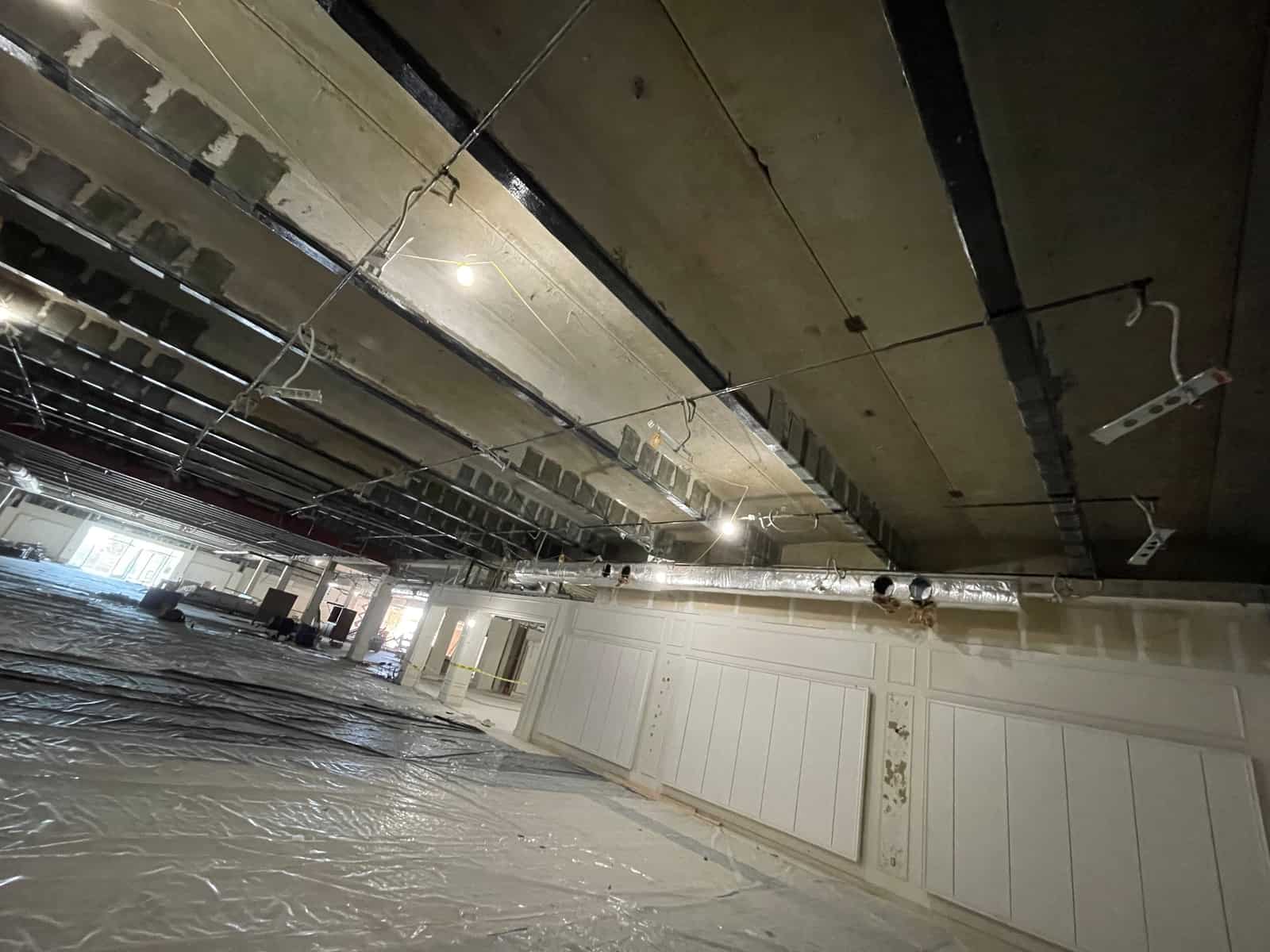 Wide view of a joist ceiling with carbon fiber bands over a plastic-covered floor.
