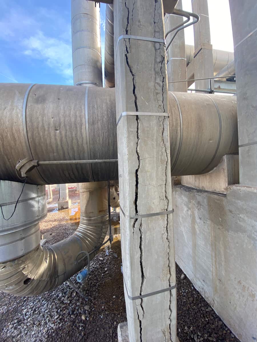 Concrete pipe-support column with long vertical cracks beside a large insulated pipe.